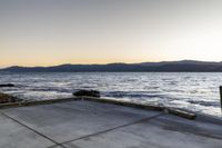 a skate boarder riding on an empty road near the water and mountain range in the distance