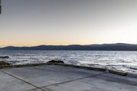 a skate boarder riding on an empty road near the water and mountain range in the distance