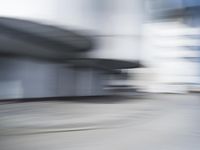 blurred photograph of a skateboarder riding on a city street in front of a building