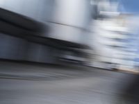 blurred photograph of a skateboarder riding on a city street in front of a building