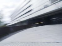 blurred photograph of a skateboarder riding on a city street in front of a building