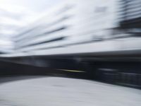 blurred photograph of a skateboarder riding on a city street in front of a building