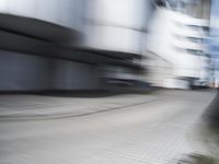 blurred photograph of a skateboarder riding on a city street in front of a building