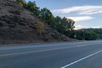 a skateboarder rides past some hills along a roadway on a cloudy day in the distance