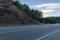 a skateboarder rides past some hills along a roadway on a cloudy day in the distance