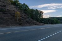 a skateboarder rides past some hills along a roadway on a cloudy day in the distance