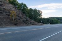 a skateboarder rides past some hills along a roadway on a cloudy day in the distance