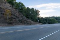 a skateboarder rides past some hills along a roadway on a cloudy day in the distance