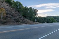 a skateboarder rides past some hills along a roadway on a cloudy day in the distance