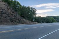 a skateboarder rides past some hills along a roadway on a cloudy day in the distance