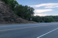 a skateboarder rides past some hills along a roadway on a cloudy day in the distance