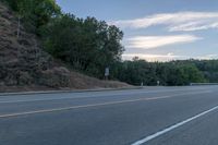 a skateboarder rides past some hills along a roadway on a cloudy day in the distance