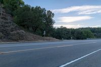 a skateboarder rides past some hills along a roadway on a cloudy day in the distance