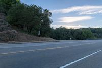 a skateboarder rides past some hills along a roadway on a cloudy day in the distance