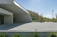 a skateboarder rides on an empty parking lot between trees and bushes in front of a building