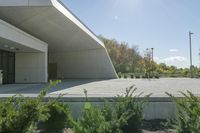 a skateboarder rides on an empty parking lot between trees and bushes in front of a building