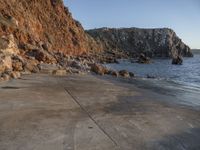 a skateboarder is doing an upside down trick by a rock wall with the ocean in the background