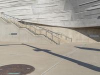 the shadow of a skateboarder on the pavement, in front of a concrete wall