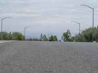 a lone skateboarder sits on the side of a road overlooking mountains and trees