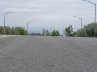 a lone skateboarder sits on the side of a road overlooking mountains and trees