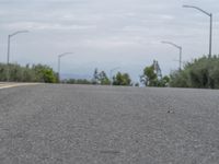 a lone skateboarder sits on the side of a road overlooking mountains and trees