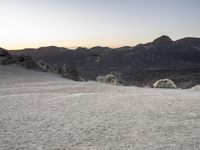 a skateboarder rides on the side of a snowy hill during sunset time with mountains in background