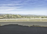 a lone skateboarder is riding along a road on a sunny day while mountains are in the background