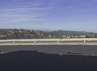 a lone skateboarder is riding along a road on a sunny day while mountains are in the background