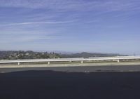 a lone skateboarder is riding along a road on a sunny day while mountains are in the background