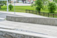 a skateboarder is doing tricks at the park, with a sidewalk below and sidewalk along the road