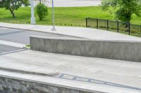 a skateboarder is doing tricks at the park, with a sidewalk below and sidewalk along the road