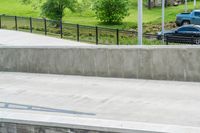 a skateboarder is doing tricks at the park, with a sidewalk below and sidewalk along the road