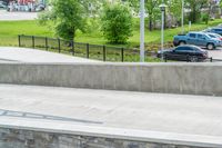 a skateboarder is doing tricks at the park, with a sidewalk below and sidewalk along the road