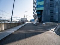 a skateboarder is going down a empty road, near a building on the edge of an urban street