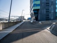 a skateboarder is going down a empty road, near a building on the edge of an urban street