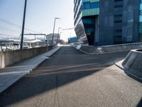 a skateboarder is going down a empty road, near a building on the edge of an urban street