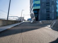 a skateboarder is going down a empty road, near a building on the edge of an urban street