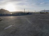 skateboarders are riding on a paved surface, near a fence and sea with a blue sky