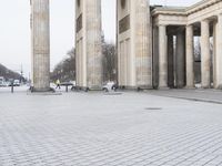 a man riding his skateboard across the middle of an outdoor plaza in front of pillars