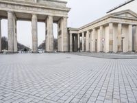 a man riding his skateboard across the middle of an outdoor plaza in front of pillars