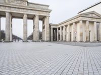 a man riding his skateboard across the middle of an outdoor plaza in front of pillars