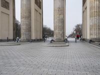 a man riding his skateboard across the middle of an outdoor plaza in front of pillars