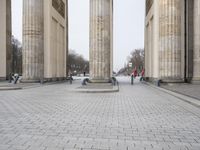 a man riding his skateboard across the middle of an outdoor plaza in front of pillars