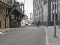 an older, empty street in a town near tall buildings and buildings, some with clock faces, and traffic signs