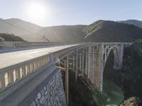 a person on a skateboard on a bridge near mountains with a view of the sun