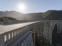 a person on a skateboard on a bridge near mountains with a view of the sun