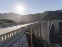 a person on a skateboard on a bridge near mountains with a view of the sun