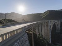 a person on a skateboard on a bridge near mountains with a view of the sun