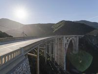 a person on a skateboard on a bridge near mountains with a view of the sun