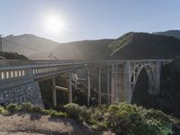 a person on a skateboard on a bridge near mountains with a view of the sun